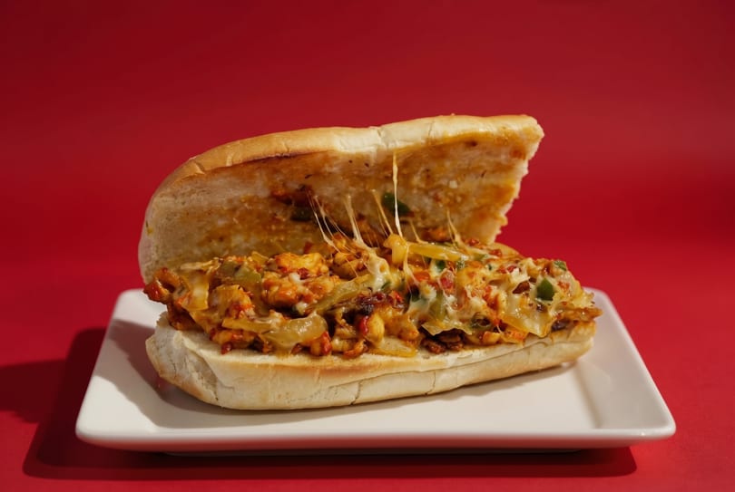 Cheesy chicken sub sandwich with melted cheese stretching, on a white plate against a red background.