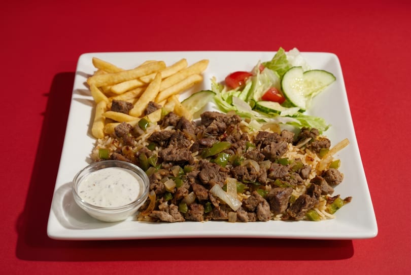 A white rectangular plate with beef and rice, fries, a side salad, and a small bowl of sauce.