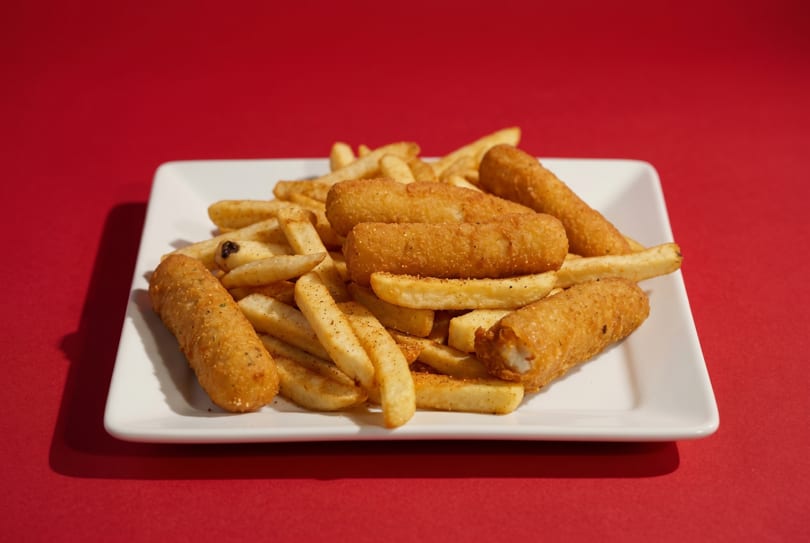 Golden-brown fish sticks and seasoned french fries on a white rectangular plate against a red background.
